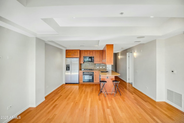 kitchen with visible vents, light wood finished floors, a sink, black appliances, and backsplash