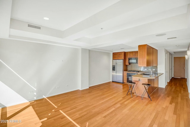 kitchen featuring visible vents, decorative backsplash, light wood-style floors, stainless steel appliances, and a sink