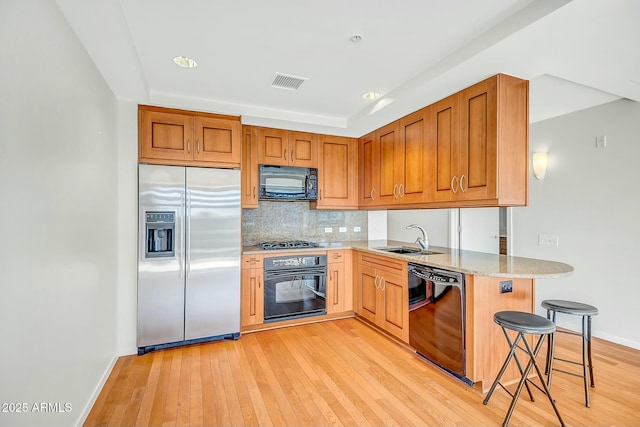 kitchen featuring visible vents, black appliances, light wood-style flooring, a sink, and backsplash