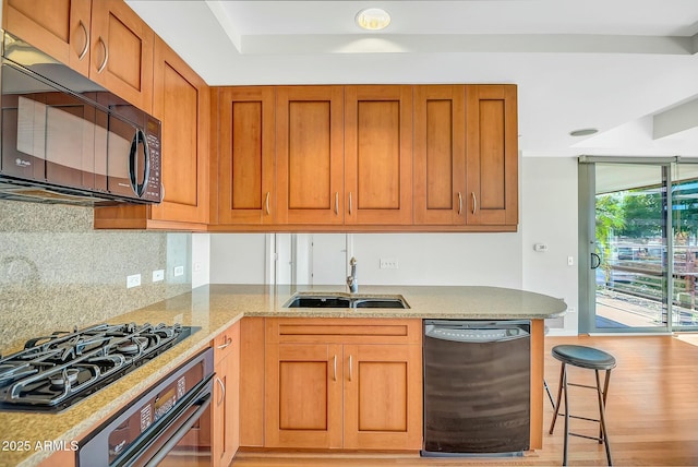 kitchen featuring light stone counters, decorative backsplash, light wood-style floors, black appliances, and a sink