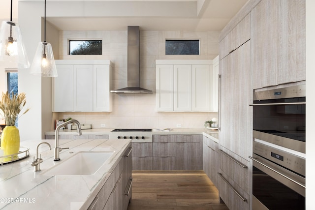 kitchen featuring appliances with stainless steel finishes, backsplash, wall chimney exhaust hood, sink, and pendant lighting