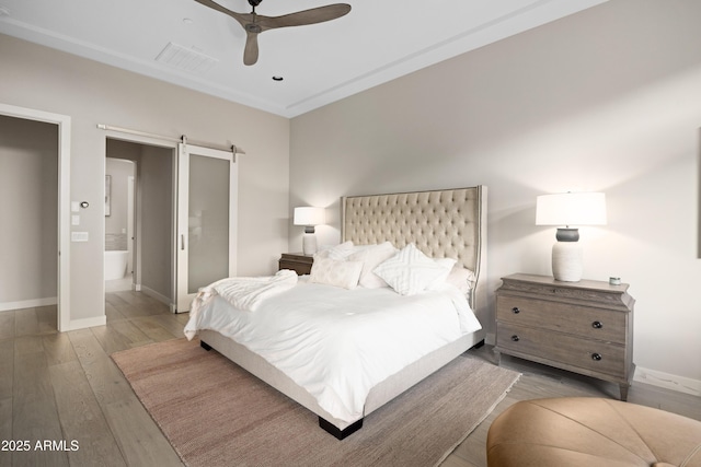 bedroom featuring ceiling fan, a barn door, connected bathroom, and light hardwood / wood-style flooring