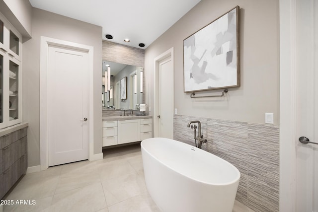 bathroom featuring tile patterned floors, a bathing tub, vanity, and tile walls