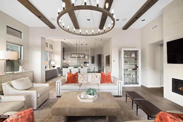 living room featuring beamed ceiling, a notable chandelier, dark wood-type flooring, and a tiled fireplace