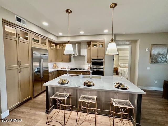 kitchen featuring wall chimney range hood, a breakfast bar, appliances with stainless steel finishes, hanging light fixtures, and a large island with sink