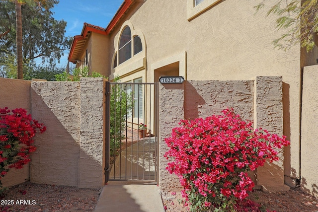 view of exterior entry with fence, a gate, and stucco siding