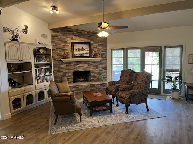 living room featuring ceiling fan, hardwood / wood-style floors, lofted ceiling with beams, and a stone fireplace