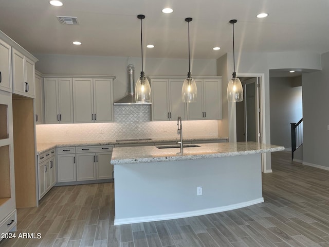 kitchen with light hardwood / wood-style flooring, hanging light fixtures, black cooktop, wall chimney exhaust hood, and sink