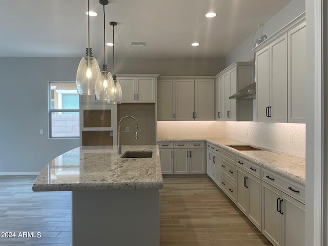 kitchen featuring black electric stovetop, a center island with sink, decorative light fixtures, sink, and tasteful backsplash