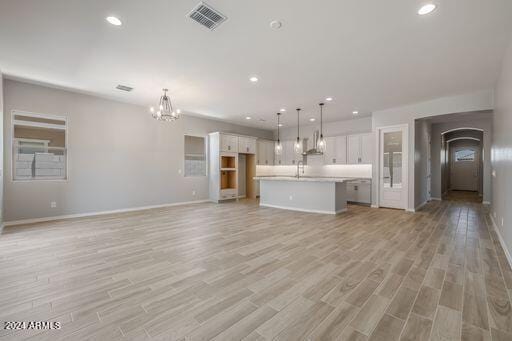 unfurnished living room with light hardwood / wood-style floors, sink, and a chandelier