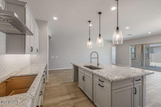 kitchen featuring hanging light fixtures, a center island with sink, light hardwood / wood-style flooring, wall chimney exhaust hood, and sink