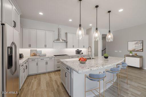 kitchen with stainless steel refrigerator with ice dispenser, light wood-type flooring, wall chimney range hood, a kitchen island with sink, and white cabinetry