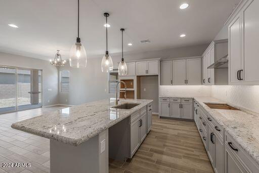 kitchen with decorative light fixtures, backsplash, a center island with sink, black electric cooktop, and sink