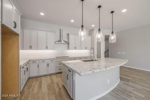 kitchen featuring wall chimney range hood, light hardwood / wood-style floors, white cabinets, sink, and pendant lighting