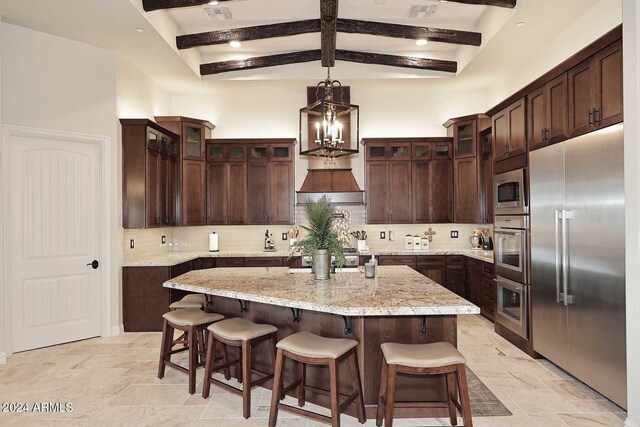 kitchen with a breakfast bar, backsplash, a kitchen island, built in appliances, and beam ceiling