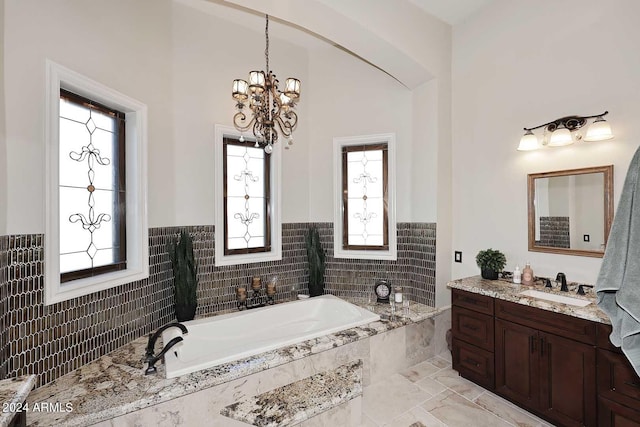 bathroom with tiled tub, vanity, a chandelier, and plenty of natural light