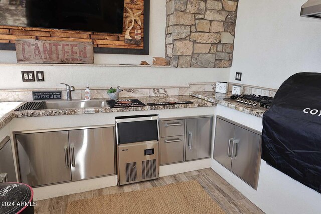 kitchen featuring gray cabinetry, light stone counters, light wood-type flooring, stainless steel gas stovetop, and sink