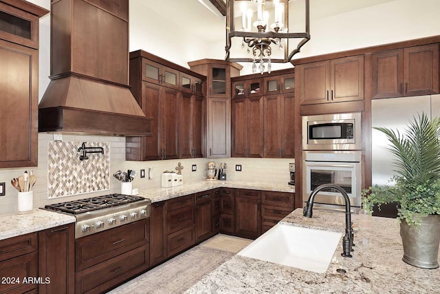 kitchen featuring light stone counters, sink, custom exhaust hood, decorative backsplash, and stainless steel appliances