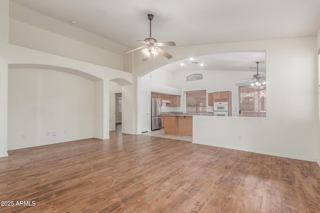 unfurnished living room with vaulted ceiling, arched walkways, ceiling fan, and light wood-style flooring