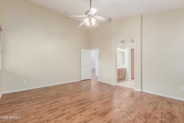 unfurnished bedroom with a towering ceiling, arched walkways, light wood-type flooring, baseboards, and ensuite bathroom
