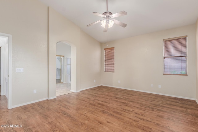 spare room with ceiling fan, arched walkways, light wood finished floors, baseboards, and lofted ceiling