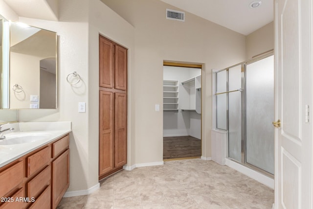 bathroom with a spacious closet, visible vents, vanity, baseboards, and a stall shower