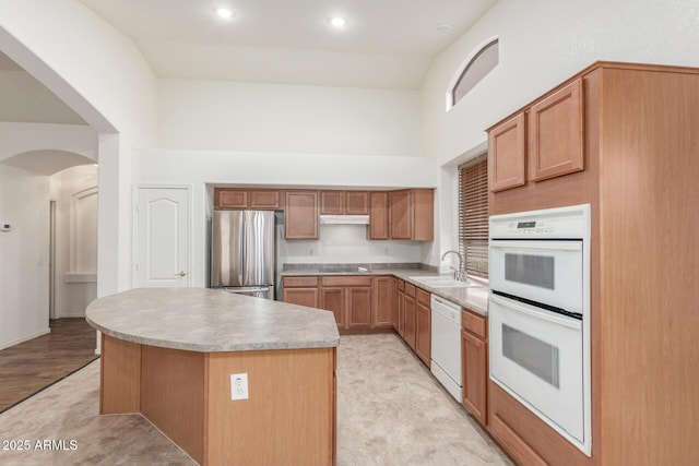 kitchen with arched walkways, a sink, a towering ceiling, white appliances, and under cabinet range hood