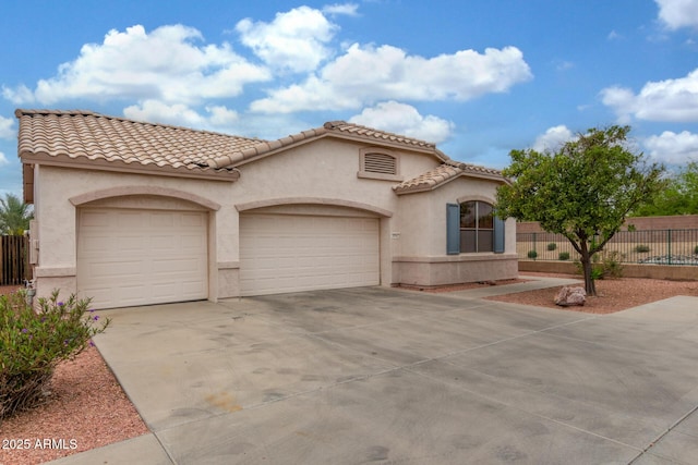 mediterranean / spanish-style home featuring fence, a tiled roof, stucco siding, an attached garage, and concrete driveway