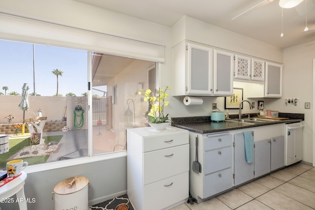 kitchen featuring dark countertops, dishwasher, a ceiling fan, light tile patterned floors, and a sink