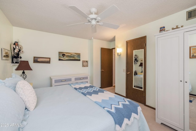 bedroom featuring visible vents, a closet, a textured ceiling, light colored carpet, and ceiling fan