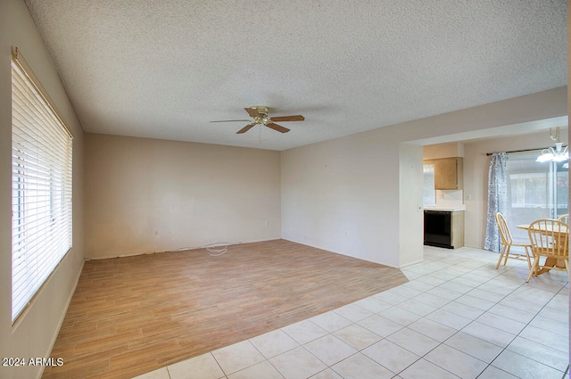 empty room featuring ceiling fan with notable chandelier, a textured ceiling, light hardwood / wood-style flooring, and a healthy amount of sunlight