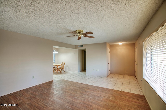 empty room with ceiling fan, light wood-type flooring, and a textured ceiling