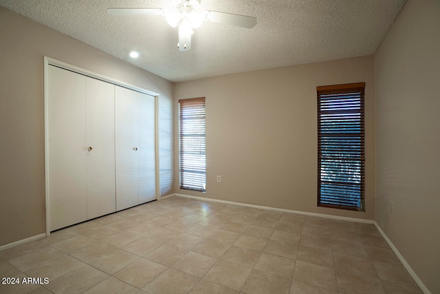 unfurnished bedroom featuring ceiling fan, a closet, light tile patterned floors, and a textured ceiling