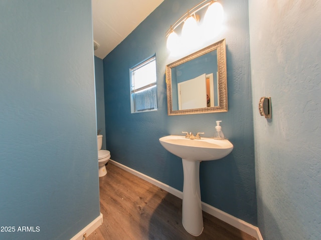half bath with baseboards, a sink, toilet, and wood finished floors