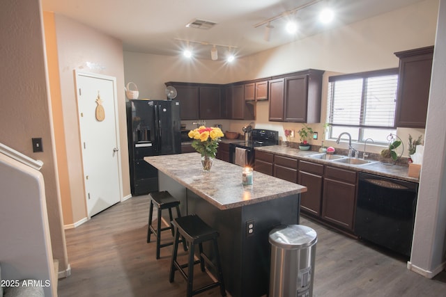 kitchen with track lighting, a center island, a sink, black appliances, and a breakfast bar area
