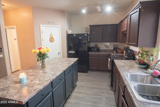 kitchen with light wood-type flooring, a center island, light countertops, black appliances, and a sink