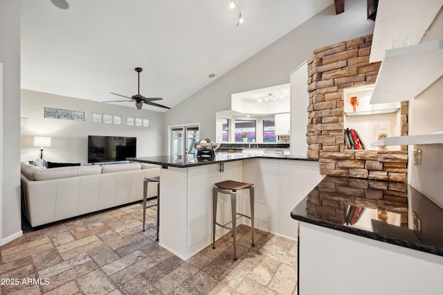 kitchen featuring high vaulted ceiling, white cabinets, a kitchen bar, ceiling fan, and kitchen peninsula