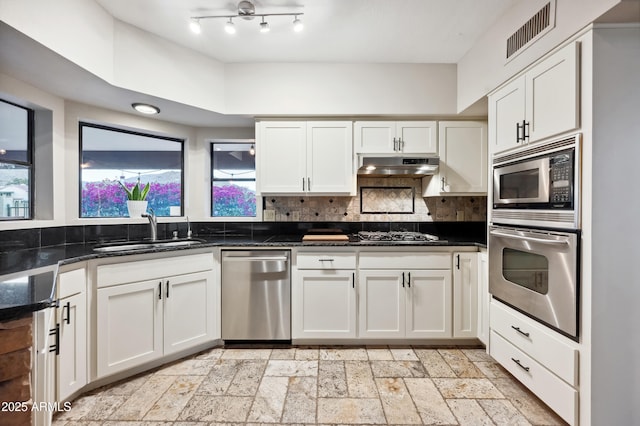 kitchen featuring sink, appliances with stainless steel finishes, dark stone countertops, white cabinetry, and backsplash