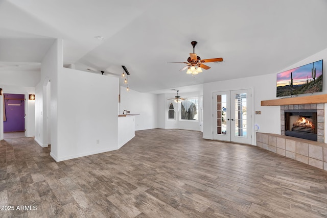 unfurnished living room with vaulted ceiling, hardwood / wood-style floors, a tiled fireplace, ceiling fan, and french doors