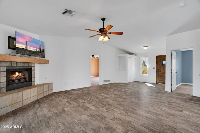 unfurnished living room featuring a tiled fireplace, vaulted ceiling, hardwood / wood-style flooring, and ceiling fan