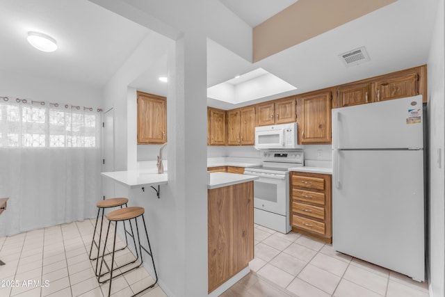 461 W Holmes Ave Unit 180, Mesa, AZ 85210 - kitchen with white appliances, light tile patterned flooring, light countertops, a kitchen breakfast bar, and brown cabinets