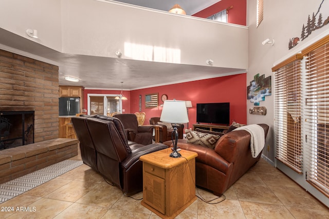 living room featuring a brick fireplace, light tile patterned flooring, crown molding, and a towering ceiling