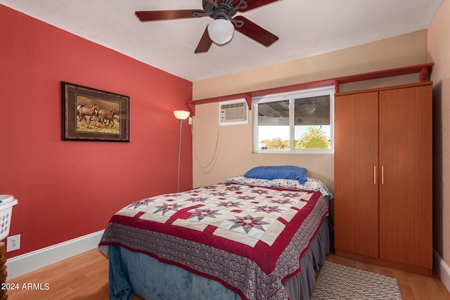 bedroom featuring a wall unit AC, light wood-type flooring, and ceiling fan