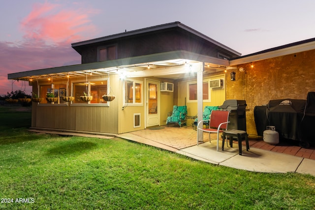 back house at dusk with a wall unit AC, a patio, and a lawn