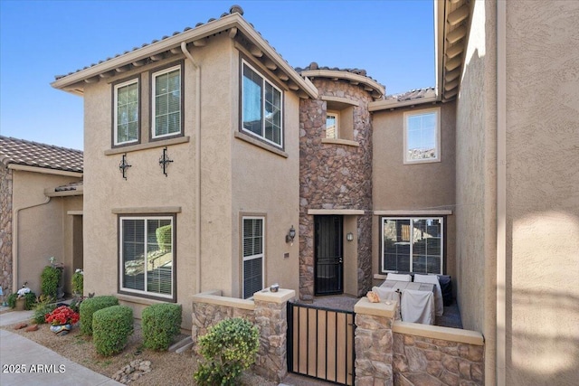back of property with stucco siding, a tiled roof, and stone siding