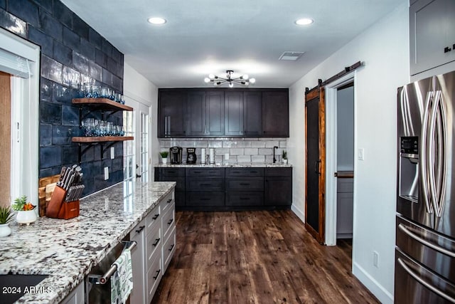 kitchen featuring stainless steel refrigerator with ice dispenser, dark hardwood / wood-style flooring, tasteful backsplash, light stone counters, and a barn door