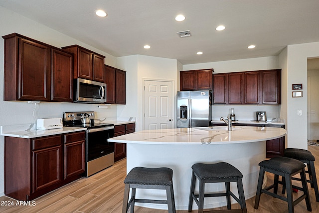 kitchen featuring light hardwood / wood-style flooring, an island with sink, stainless steel appliances, sink, and a breakfast bar