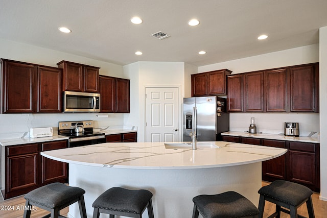 kitchen featuring stainless steel appliances, a center island with sink, hardwood / wood-style flooring, and a kitchen bar