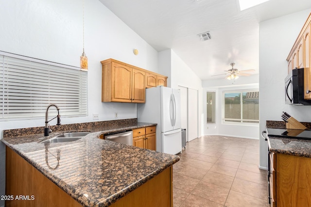 kitchen with dark stone countertops, vaulted ceiling, sink, decorative light fixtures, and stainless steel appliances