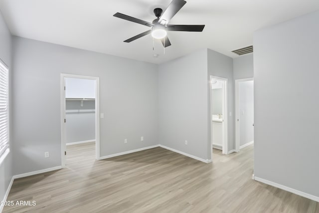unfurnished bedroom featuring a spacious closet, baseboards, light wood-style floors, visible vents, and a ceiling fan